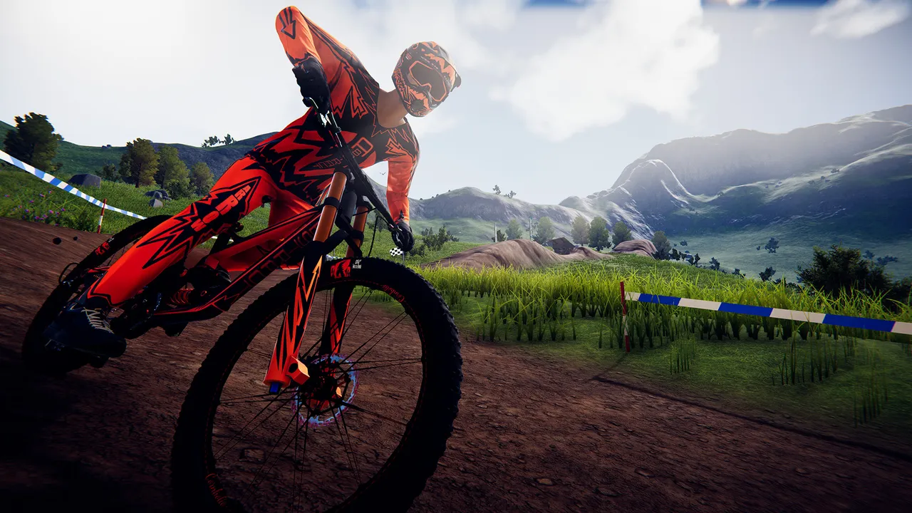 Descenders: a rider in orange gear on a dirt track in green highlands with taped course markers and mountains