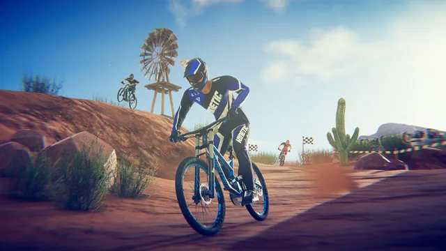 Descenders: a rider in blue gear on a desert track with a windmill, a cactus and other riders behind