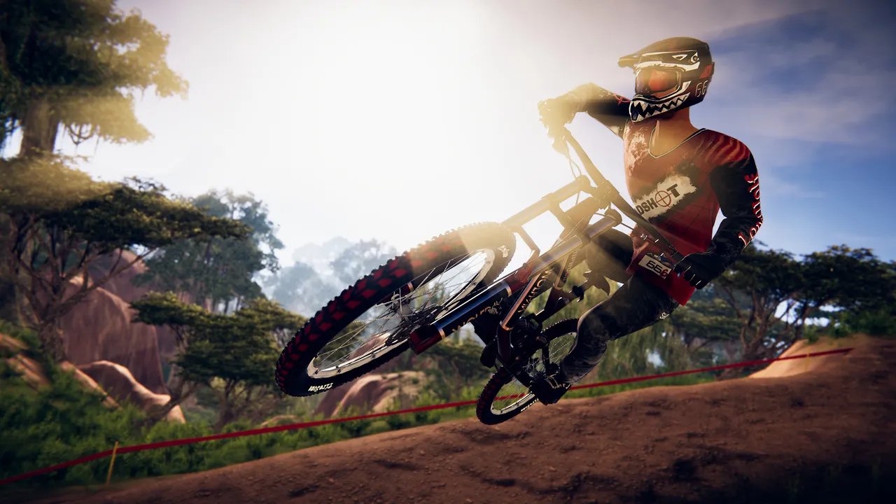 Descenders: a rider in red gear leaning the bike through a jump on a sunlit forest track