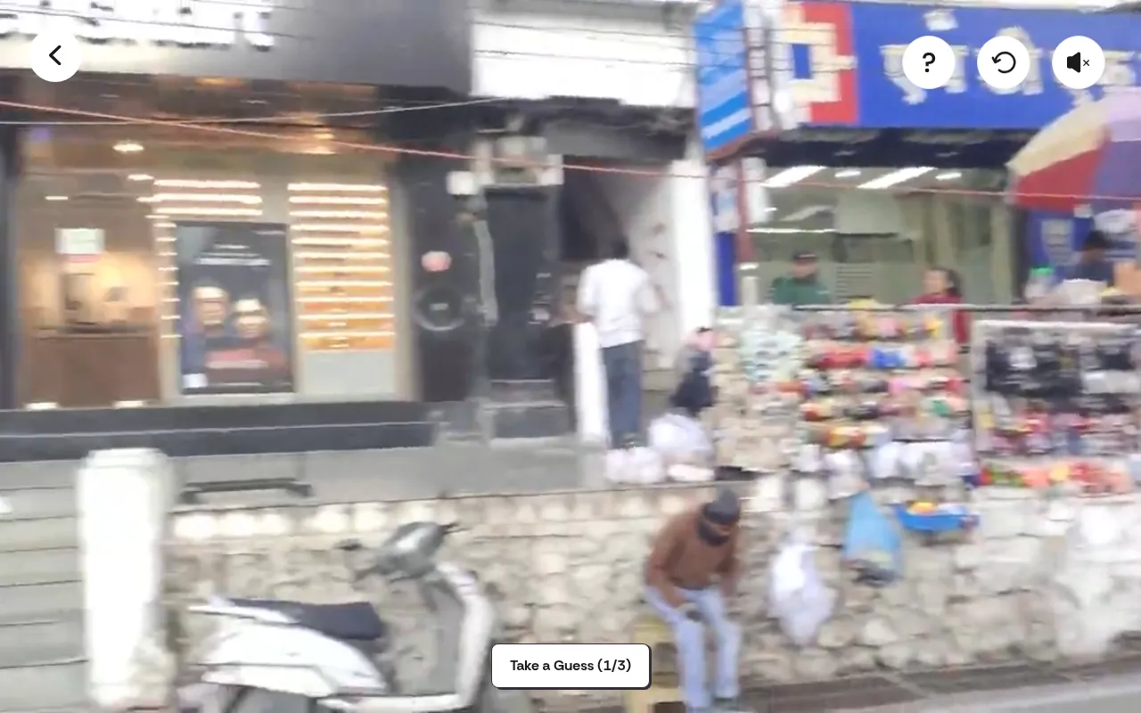 Location Guesser's daily video playing: a busy Indian street with shop fronts and a market stall, with the Take a Guess (1/3) button below