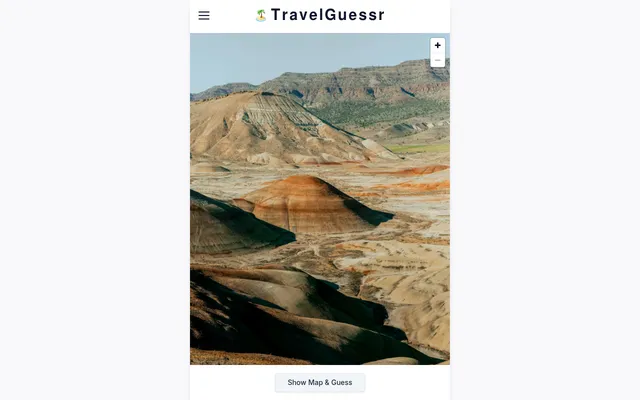 Today's first TravelGuessr round: a photo of striped red and tan hills under a ridge, with zoom buttons and the Show Map & Guess button