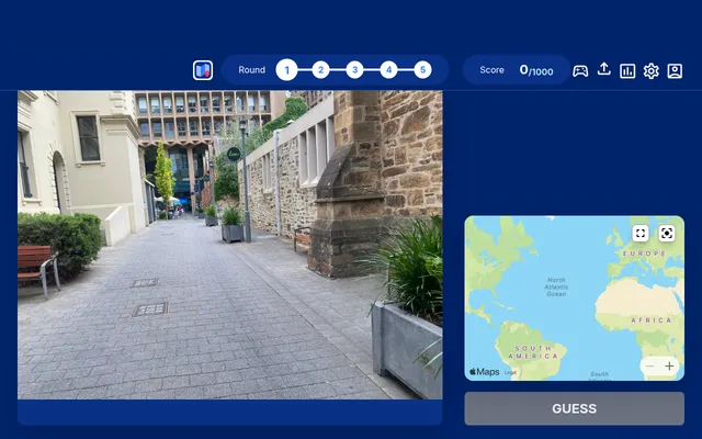 WhereTaken round 1 of 5: a street photo of a paved lane between stone buildings, beside the world map to place a pin on and the Guess button, score 0 of 1000